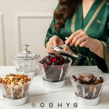 Person in a green robe selecting snacks from glass containers on a table, with 'SOBHYS' branding. Sobhys Luxury Crystal Bowl – Silver-Tone Ribbed Finial Handle Close-Up
